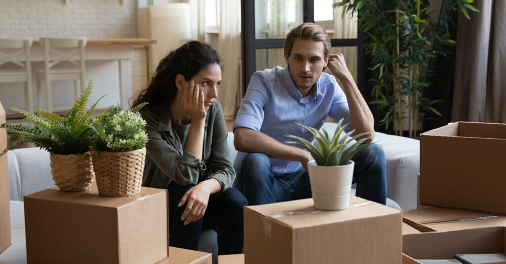 Confused homebuyers in new home, surrounded by boxes and plants